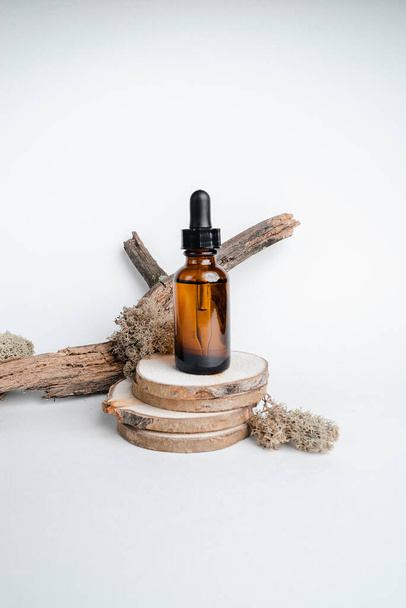 Dark glass bottles stand on wooden cuts, next to  branch. Monochrome photography trend. Isolate on white background. Place for text. Bottle of Spa essential oil for aromatherapy  - Foto, Imagen