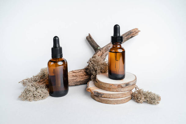 Dark glass bottles stand on wooden cuts, next to  branch. Monochrome photography trend. Isolate on white background. Place for text. Bottle of Spa essential oil for aromatherapy  - Foto, Imagem