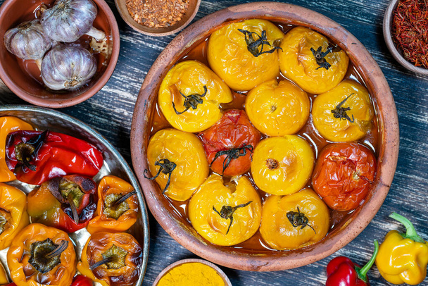 Baked red and yellow tomato and bell pepper. Tomatoes and bell peppers in a baking dish on a wooden table. A healthy and delicious vegetarian dish. Close up, top view - Photo, image