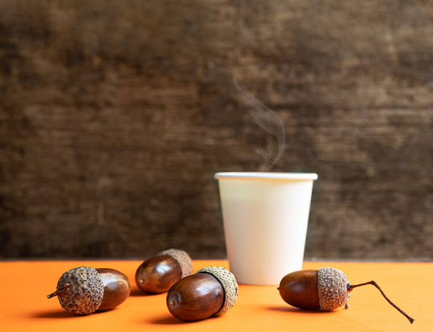 Kartónový šálek z ekologického materiálu se žaludy kávy a žaludy na oranžovém stole. Zdravý život bez kofeinu a plastu zdarma koncept - Fotografie, Obrázek