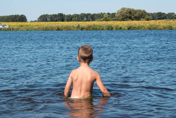 αγόρι στέκεται στο νερό στο φόντο ενός κίτρινου πεδίου - Φωτογραφία, εικόνα