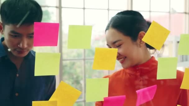Business people work on project planning board in office and having conversation with coworker friend to analyze project development . They use sticky notes posted on glass wall to make it organized . - Footage, Video