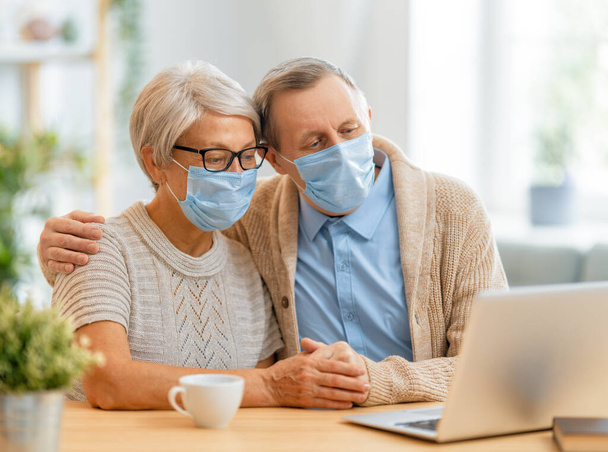 Senior couple wearing facemasks and using pc during coronavirus and flu outbreak. Virus and illness protection, home quarantine. COVID-2019. Taking on or taking off masks. - Φωτογραφία, εικόνα