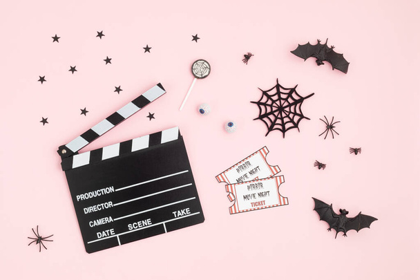 Filmklappbrett und Halloween-Dekoration auf rosa Hintergrund. Horrorfilmabend, Halloween-Party-Einladung. Draufsicht, Kopierraum, Attrappe - Foto, Bild
