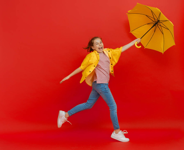 Boldog érzelmi gyerek nevet és ugrál. Gyerek sárga esernyő színes piros háttér. - Fotó, kép