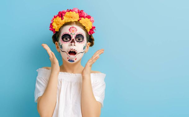 Adorable zombie in flower wreath posing on blue background. Happy child with Halloween creative makeup. Girl celebrating for Mexican Day of the Dead. - Zdjęcie, obraz