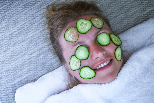 Caucasian woman mask cosmetic mask and cucumber patches face for beauties at home. Female lying on couch home and doing restoring face masks portrait. Healthy facial skin care at home help concept. Woman applying homemade facial mask - Photo, Image