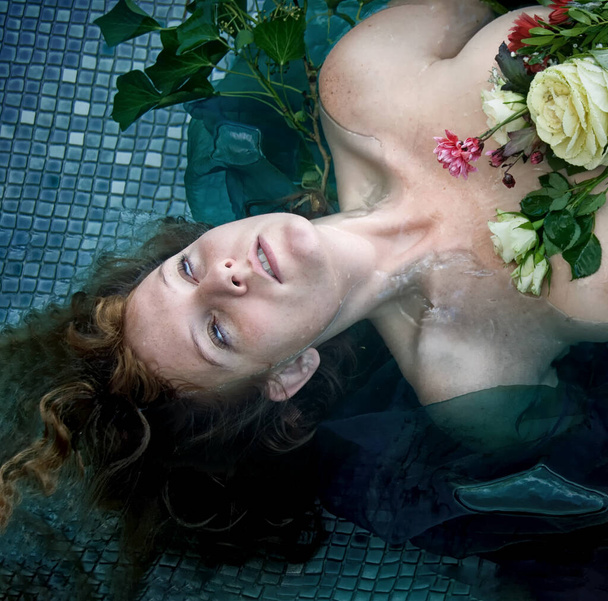 retrato de jovem sexy infeliz mulher louca senhora Ofélia com cabelo encaracolado vermelho encontra-se com as flores com olhos mortos na água na piscina, espaço cópia - Foto, Imagem