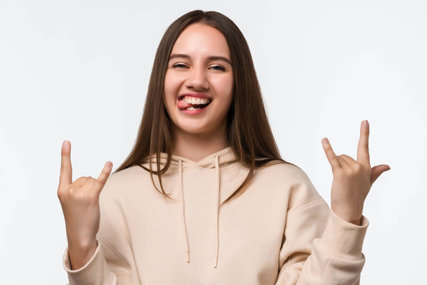 Emotive Young woman with blonde straight hair straight hair makes ROCK N ROLL sign, says: I will rock this party, wearing stylish beige hoodie, feels self confident. Human emotions concept - Photo, Image