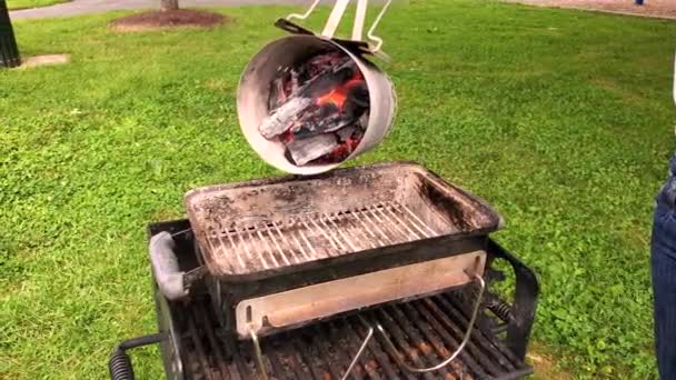 Een vrouw verplaatst hete brandende steenkoolklompen in een tuingrill van een schoorsteen starter. Dit is een cilindrisch metalen gereedschap met handvat dat wordt gebruikt om steenkoolklontjes en briketten te ontsteken voor de barbecue. - Video