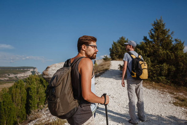 Két férfi mászkál a sziklás lejtőn hátizsákokat cipelve túrázó botokkal. Hegyek völgye Kilátás az emberek mellett. nyári kirándulás a természetbe. Túrázó a háttérben. - Fotó, kép