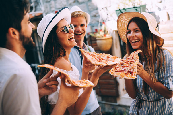 Друзья веселятся на свежем воздухе, едят пиццу на летних каникулах - Фото, изображение