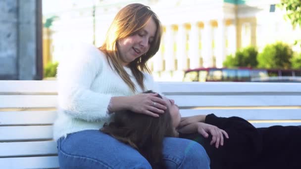 Lesbische liggend op de bank en de knieën van haar vriendin in het park. De media. Lesbische vrouw zoenen een ander meisje op haar voorhoofd, lachen op een date, lgbt concept. - Video