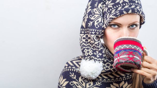 Cheerful young woman in christmas outfit knitted hat and sweater holding hot drink isolated over white - Valokuva, kuva