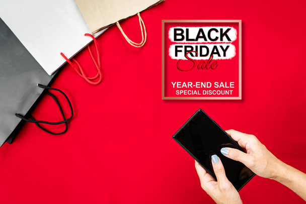 noir vendredi vente, femme main achats en ligne sur smartphone avec sac à provisions sur fond rouge - Photo, image
