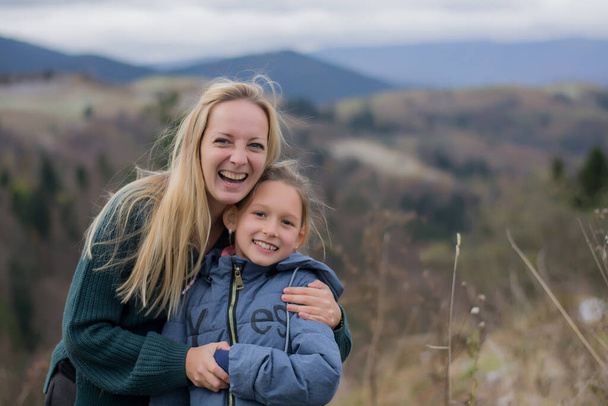 Mom and daughter are smiling and hugging in the mountains. Parent and child travel in the autumn mountains. Carpathian mountains - Zdjęcie, obraz
