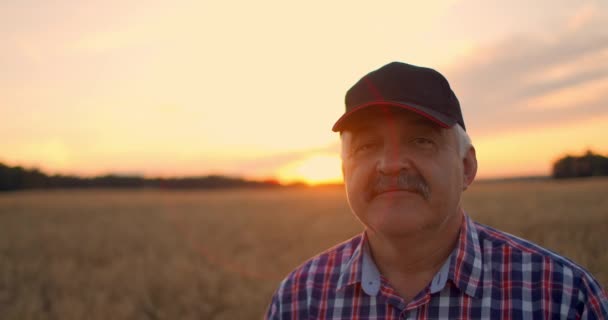 Close-up portret van een boer in een pet bij zonsondergang die recht in de camera kijkt  - Video
