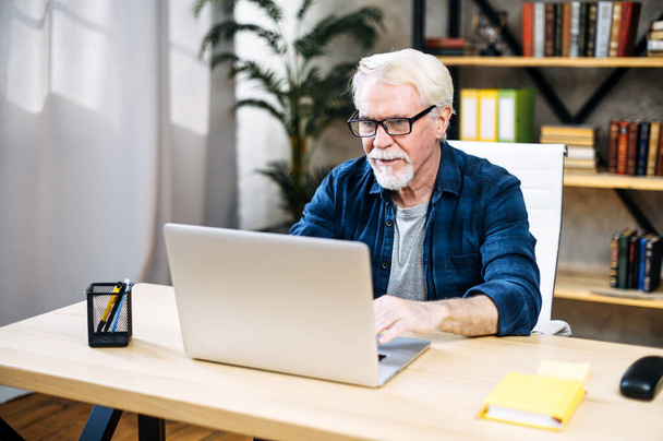 Older man is using laptop for working indoor - Foto, afbeelding