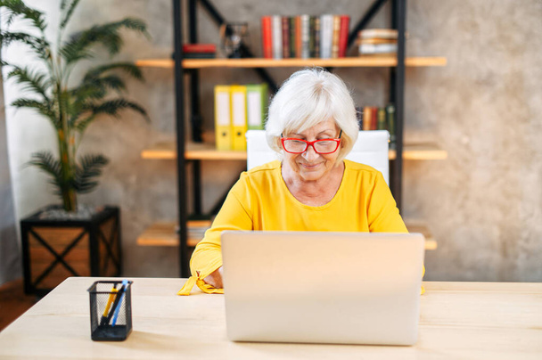 Senior woman is using laptop for work indoor - Foto, Imagen