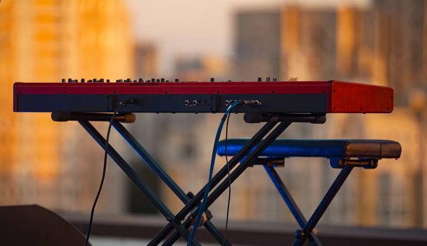 Κοντινή φωτογραφία του ηλεκτρονικού κόκκινου πιάνου που κάθεται στην ταράτσα, ώρα πριν από τη συναυλία - Φωτογραφία, εικόνα