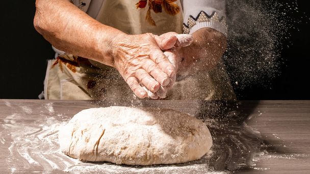 Foto de harina y manos de mujeres con salpicadura de harina. Cocinar pan. Amasar la masa. Aislado sobre fondo oscuro. Espacio vacío para texto. - Foto, Imagen