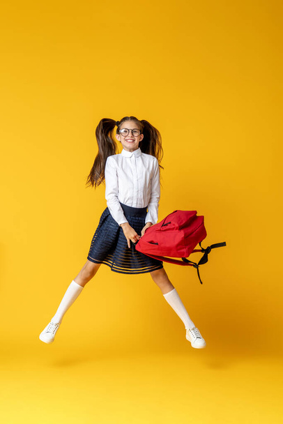 mischievous schoolgirl in glasses, uniform with backpack and books jumps on yellow background. Dynamic images that go back to conceptual school. holidays begin. Back to school. girl is ready to study - Foto, immagini