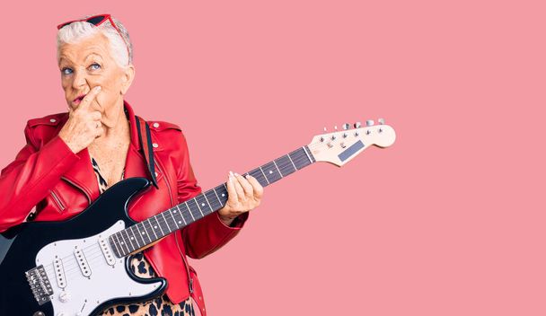 Senior όμορφη γυναίκα με μπλε μάτια και γκρίζα μαλλιά φορώντας ένα μοντέρνο βλέμμα παίζει ηλεκτρική κιθάρα σκέφτεται ανησυχούν για μια ερώτηση, ανησυχούν και νευρικό με το χέρι στο πηγούνι  - Φωτογραφία, εικόνα