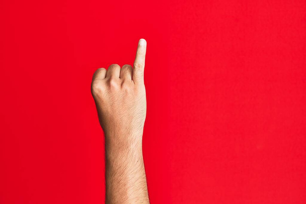 Arm of caucasian white young man over red isolated background showing little finger as pinky promise commitment, number one  - Photo, Image