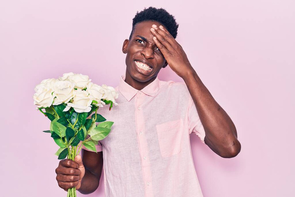 Fiatal afro-amerikai férfi kezében virágok stresszes és frusztrált a kezét a fejre, meglepett és dühös arc  - Fotó, kép