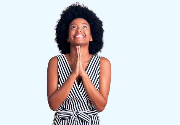 Joven mujer afroamericana vestida con ropa casual mendigando y rezando con las manos juntas con expresión de esperanza en la cara muy emotiva y preocupada. mendicidad.  - Foto, Imagen