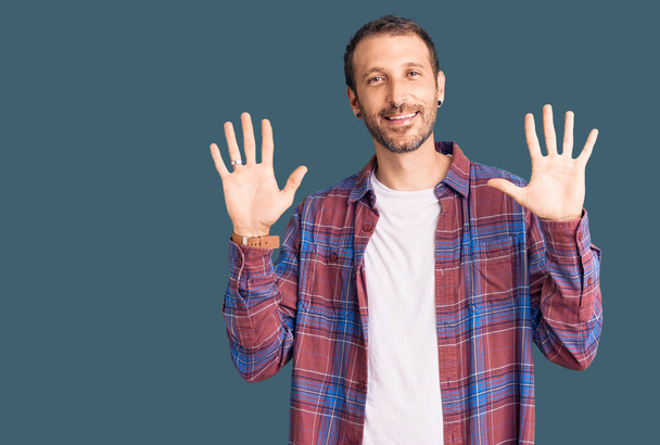 Junger gutaussehender Mann in lässiger Kleidung zeigt mit Finger Nummer zehn nach oben und lächelt dabei selbstbewusst und glücklich.  - Foto, Bild