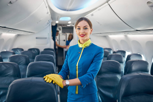 Молодая красивая стюардесса, стоящая в проходе пассажирского салона самолета - Фото, изображение