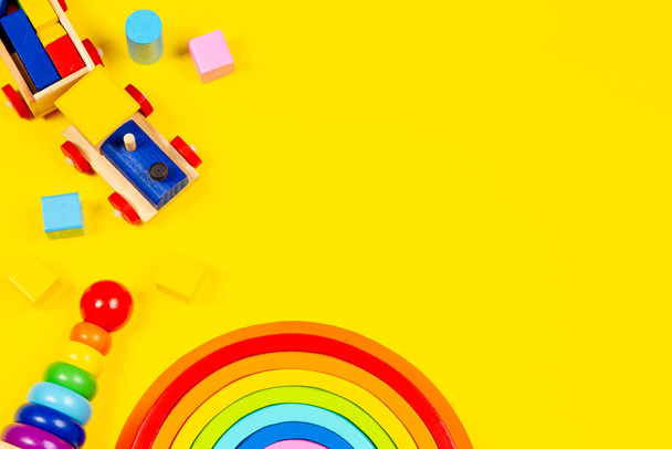 Baby kid toys background. Wooden toy train, wood rainbow and colorful blocks on yellow background. Top view, flat lay - Foto, immagini