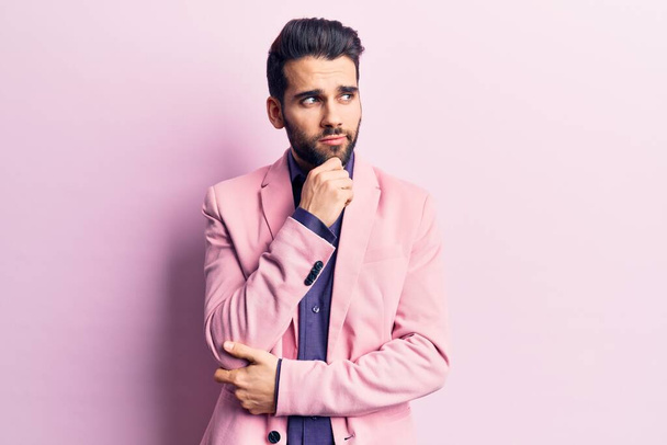 Young handsome man with beard wearing elegant jacket with hand on chin thinking about question, pensive expression. smiling with thoughtful face. doubt concept.  - Foto, afbeelding