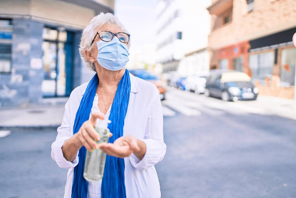 Vanhempi vanhempi nainen harmaat hiukset yllään coronavirus turvallisuus naamio ja käyttämällä sanitizer geeli ulkona - Valokuva, kuva