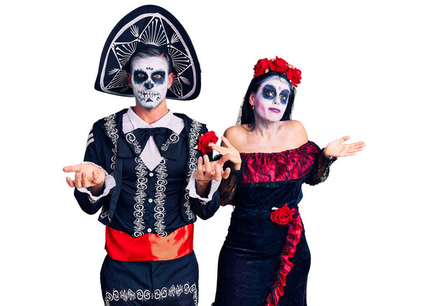 Młoda para ubrana w meksykański dzień martwego kostiumu na tle nieświadoma i zdezorientowana z otwartymi ramionami, bez pojęcia.  - Zdjęcie, obraz
