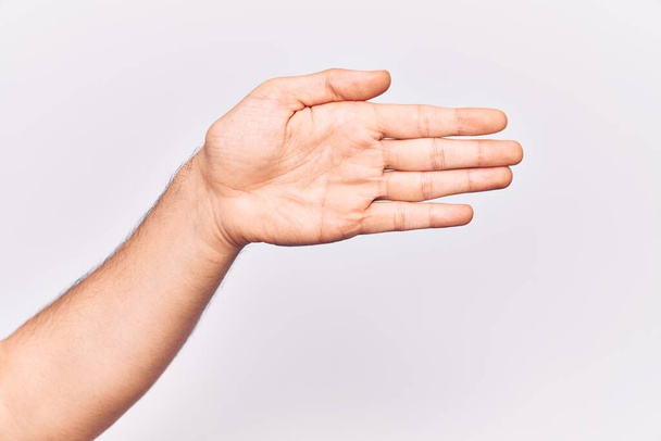 Primer plano de la mano del joven caucásico sobre fondo aislado estirándose y alcanzando con la mano abierta para apretón de manos, mostrando la palma  - Foto, Imagen