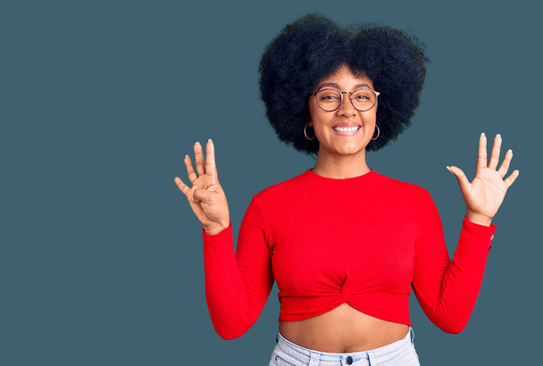 Chica afroamericana joven con ropa casual y gafas mostrando y apuntando hacia arriba con los dedos número nueve mientras sonríe confiado y feliz.  - Foto, Imagen