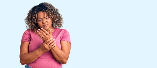 Jovem afro-americana plus size mulher vestindo roupas casuais sofrendo dor nas mãos e dedos, artrite inflamação  - Foto, Imagem