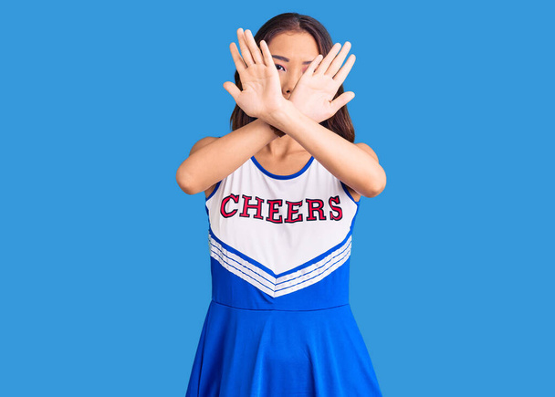 Giovane bella ragazza cinese indossa cheerleader espressione di rifiuto uniforme incrociando le braccia facendo segno negativo, faccia arrabbiata  - Foto, immagini