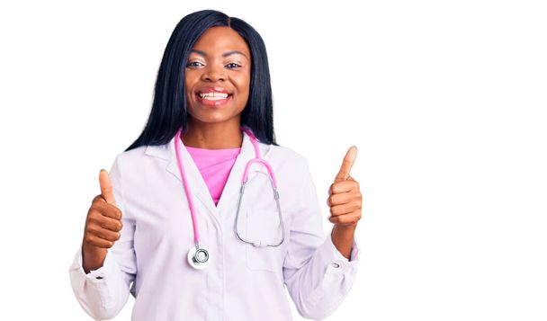 Genç Afro-Amerikan kadın doktor steteskobu takıyor. Elleriyle olumlu jest yapıyor. Gülümsüyor ve mutlu. Neşeli ifade ve kazanan jest.  - Fotoğraf, Görsel