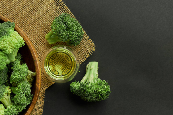 Fresh Broccoli in wooden bowl and seed oil in rustic style. Close up on a black background. copy space for text. Top view, flat lay. - Photo, Image