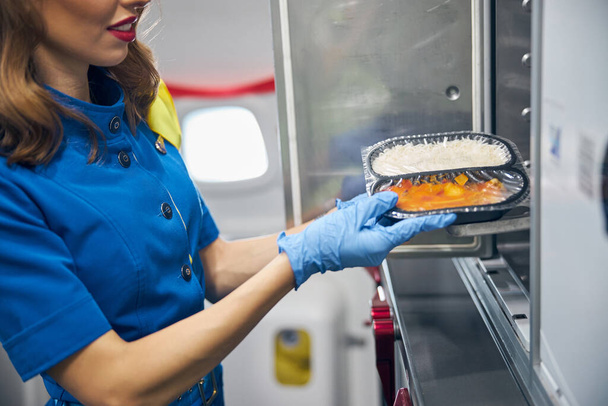 民間航空機のキッチンで乗客に食事を提供するスチュワーデス - 写真・画像