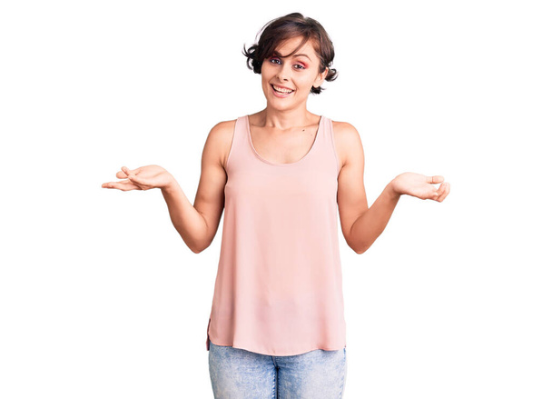 Beautiful young woman with short hair wearing casual style with sleeveless shirt clueless and confused expression with arms and hands raised. doubt concept.  - Photo, Image