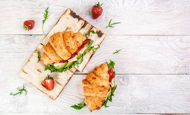 Breakfast, business lunch, sandwiches Croissant with strawberries and soft cheese with mold brie camembert on wooden background. banner menu recipe top view. - Photo, Image