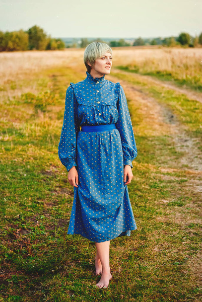 Νεαρή κομψή ευτυχισμένη κυρία με μπλε φόρεμα που περπατά στη φύση - Φωτογραφία, εικόνα