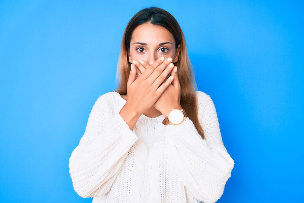 カジュアルなセーターを着た若いブルネットの女性は間違いのために手で口を覆いショックを受けた。秘密の概念.  - 写真・画像