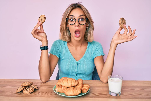 Beautiful caucasian woman sitting on the table eating breakfast afraid and shocked with surprise and amazed expression, fear and excited face.  - Photo, Image