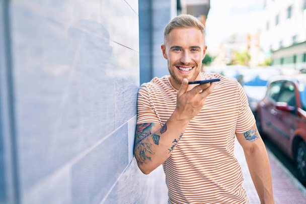 Молодой ирландец улыбается счастливо разговаривая по смартфону на улице города. - Фото, изображение