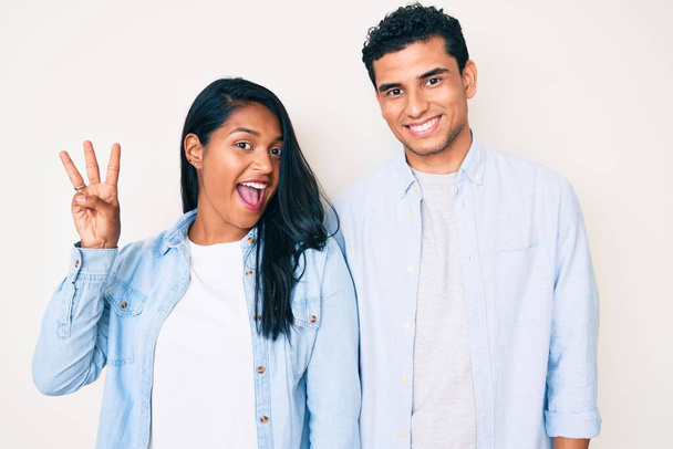 Bella latina giovane coppia indossa abiti casual mostrando e indicando con le dita numero tre, mentre sorridente fiducioso e felice.  - Foto, immagini